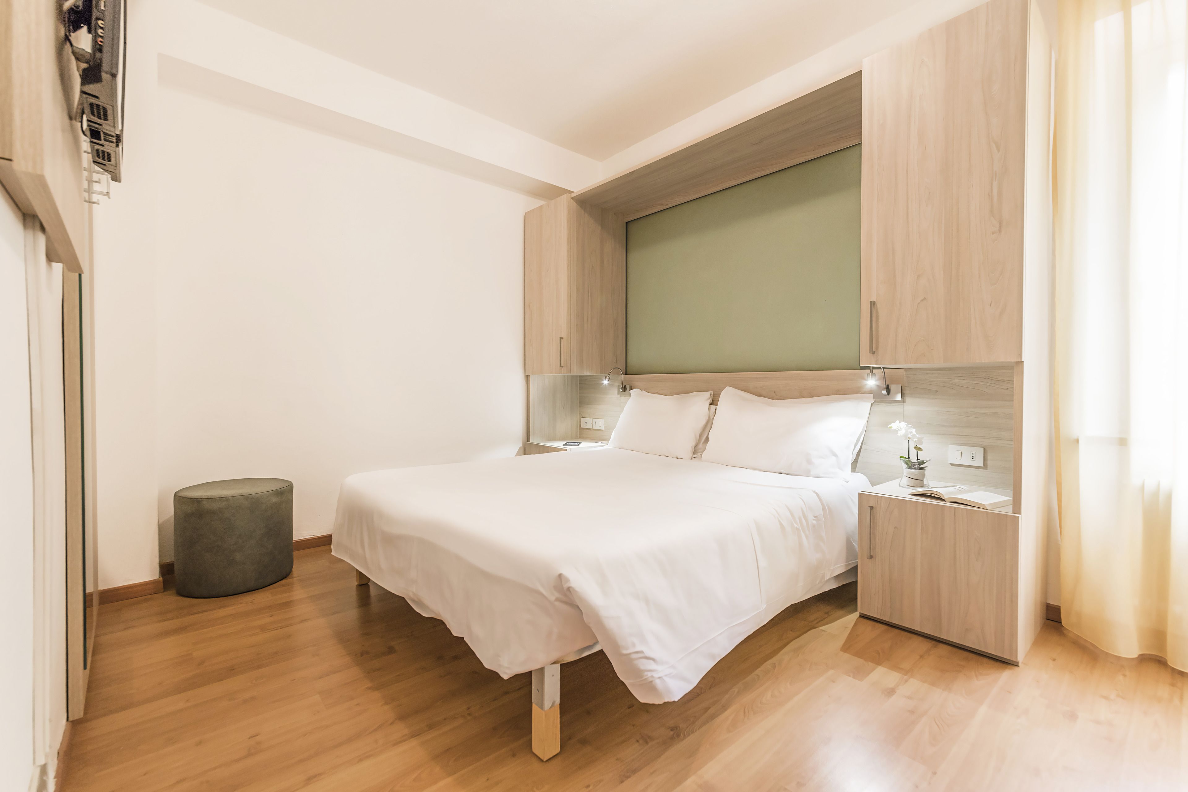 Una camera da letto con un letto, comodini, un piccolo sgabello e armadi a muro in legno.