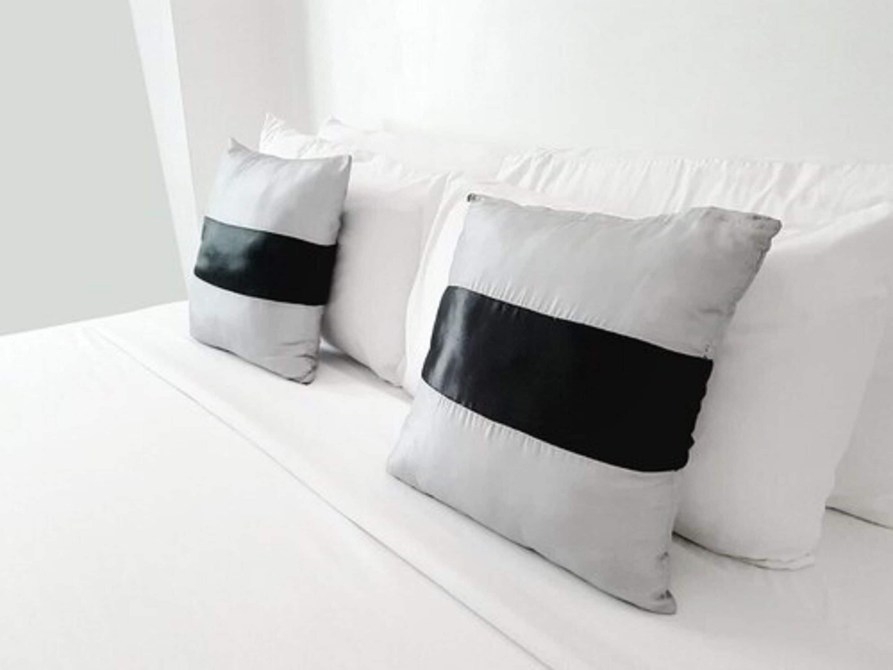 A bed with white bedding and two pillows with black bands.