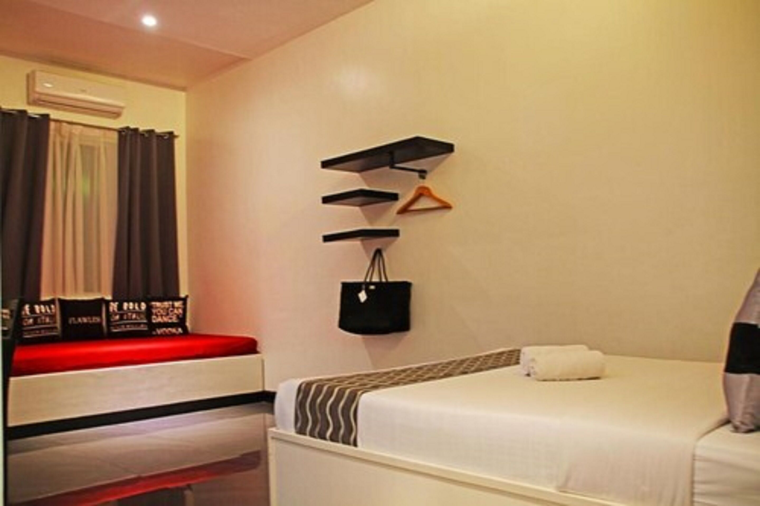 A hotel room with a bed, a small desk, and a wall-mounted shelf with a handbag and a hanger.