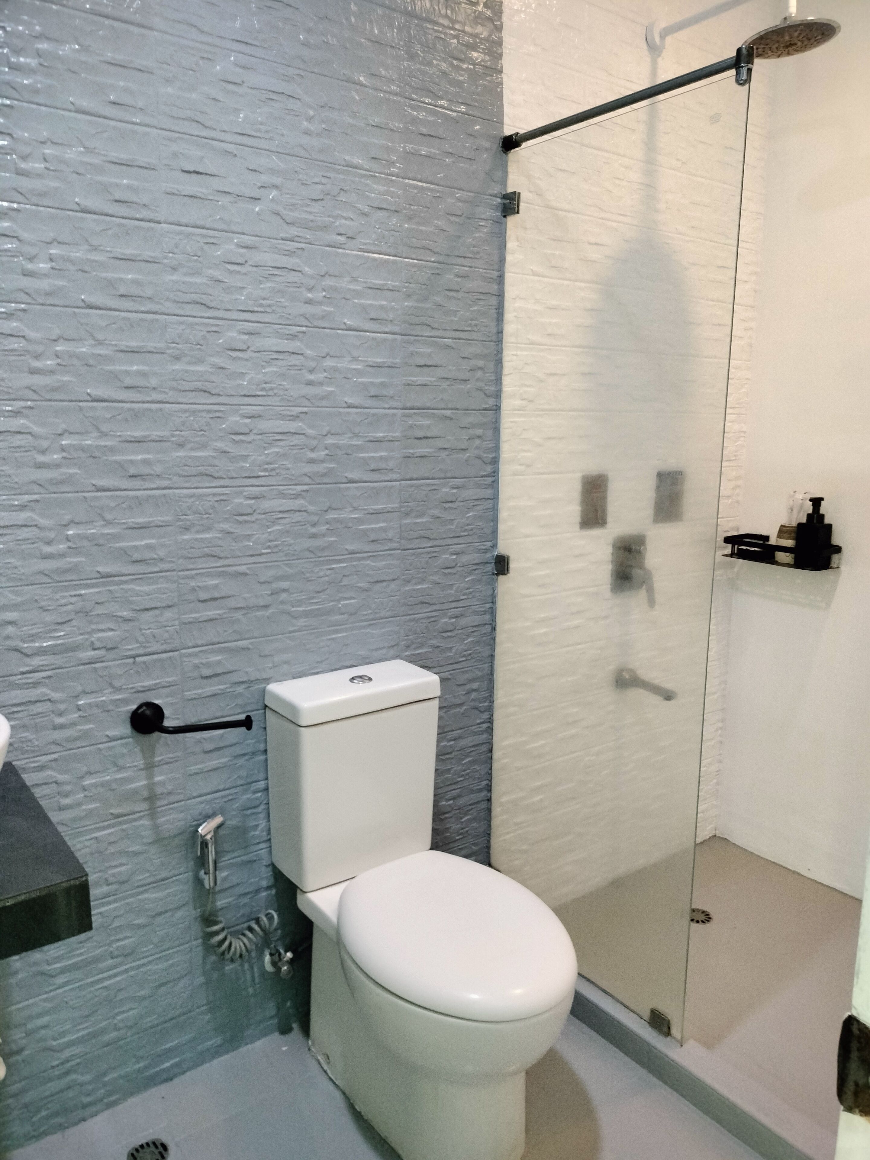 Un baño moderno con inodoro blanco, cabina de ducha con paredes de vidrio y pared gris con textura.