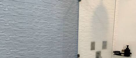 Un baño moderno con inodoro blanco, cabina de ducha con paredes de vidrio y pared gris con textura.