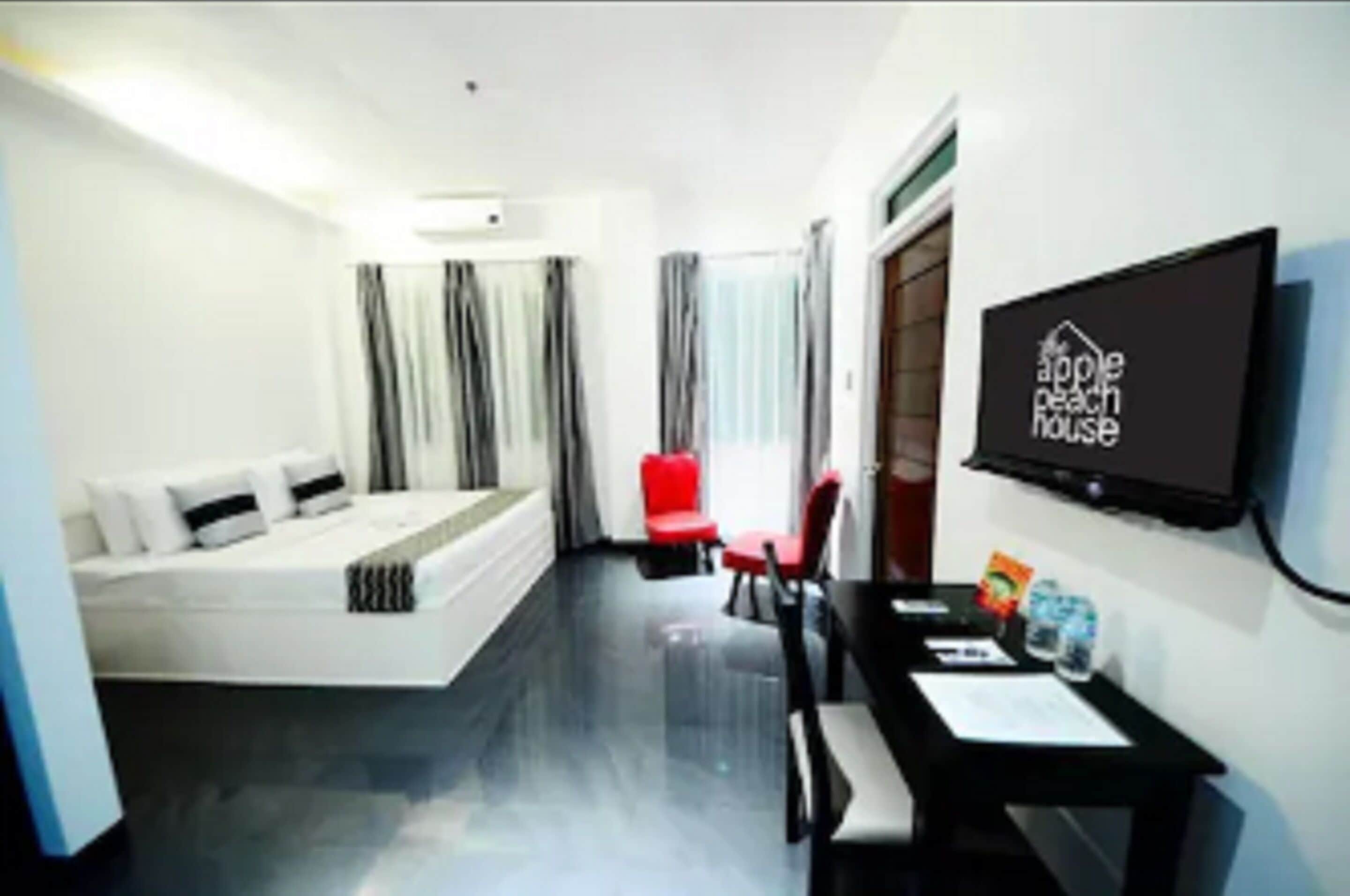 A hotel room with a bed, a desk, a chair, a TV, and a window with curtains.