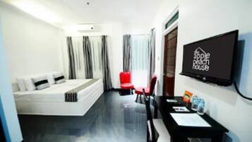 A hotel room with a bed, a desk, a chair, a TV, and a window with curtains.