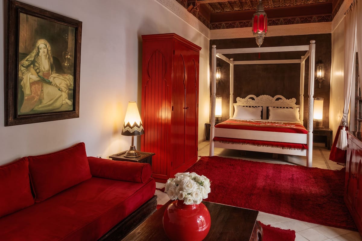 Une chambre avec un lit à baldaquin, des meubles rouges, un tableau au mur et un lustre.