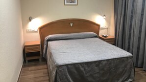 A hotel room with a wooden headboard, a bed with a grey bedspread, two bedside lamps, a nightstand with a phone, and a framed picture on the wall. - Hotel La Unión (Humanes de Madrid)
