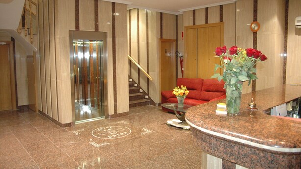 A hotel lobby with a reception desk, a red sofa, a staircase, and an elevator. - Hotel La Unión (Humanes de Madrid)