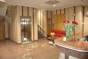 A hotel lobby with a reception desk, a red sofa, a staircase, and an elevator. - Hotel La Unión (Humanes de Madrid)