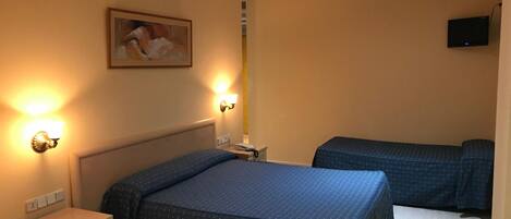 A hotel room with two beds, a desk, a chair, a nightstand, a wall-mounted TV, and a painting on the wall.
