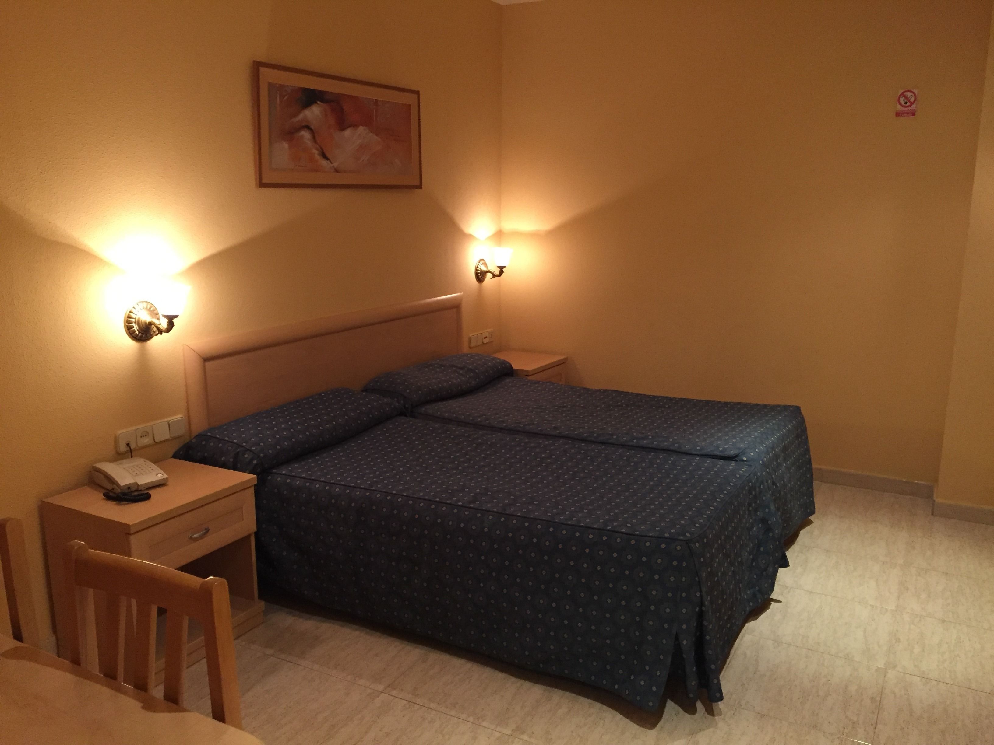 A hotel room with a bed, bedside tables, a desk, and a chair.