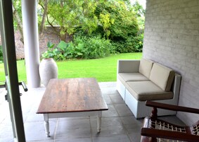 An outdoor patio with a wooden table, a wicker sofa, and a large planter.