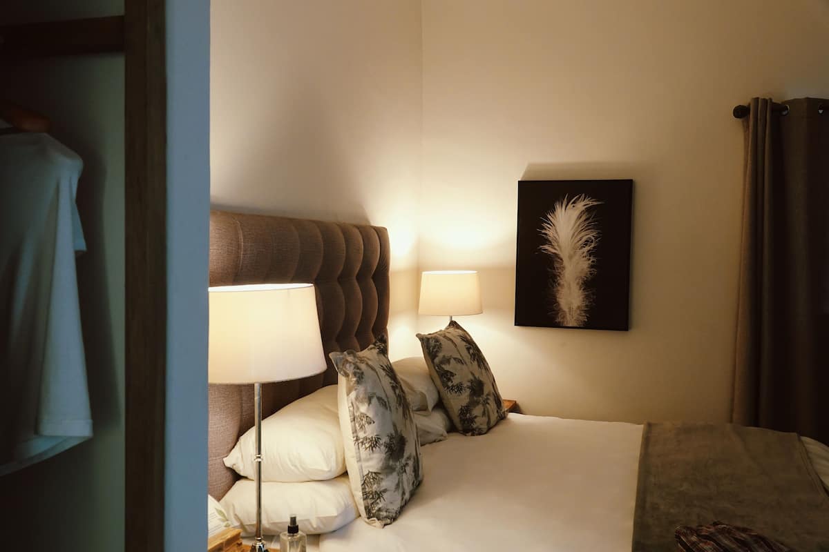 Une chambre d’hôtel avec un lit, deux lampes de chevet, une œuvre d’art en plumes accrochée au mur et une tête de lit marron.