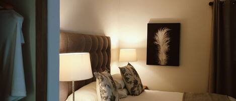Ein Hotelzimmer mit einem Bett, zwei Nachttischlampen, einem Wandbild aus Federn und einem braunen Kopfteil.