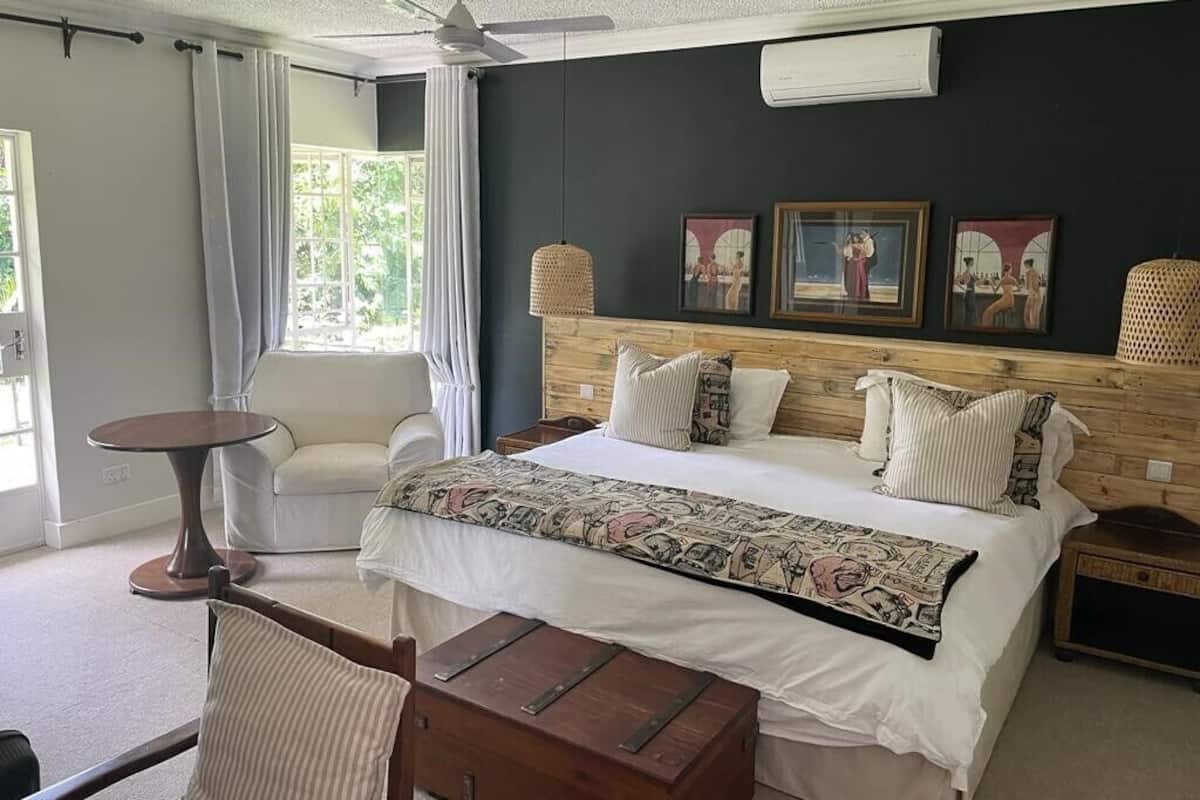 Une chambre à coucher avec un lit, une chaise, une petite table et une commode en bois. Il y a trois tableaux encadrés au mur et un ventilateur de plafond.