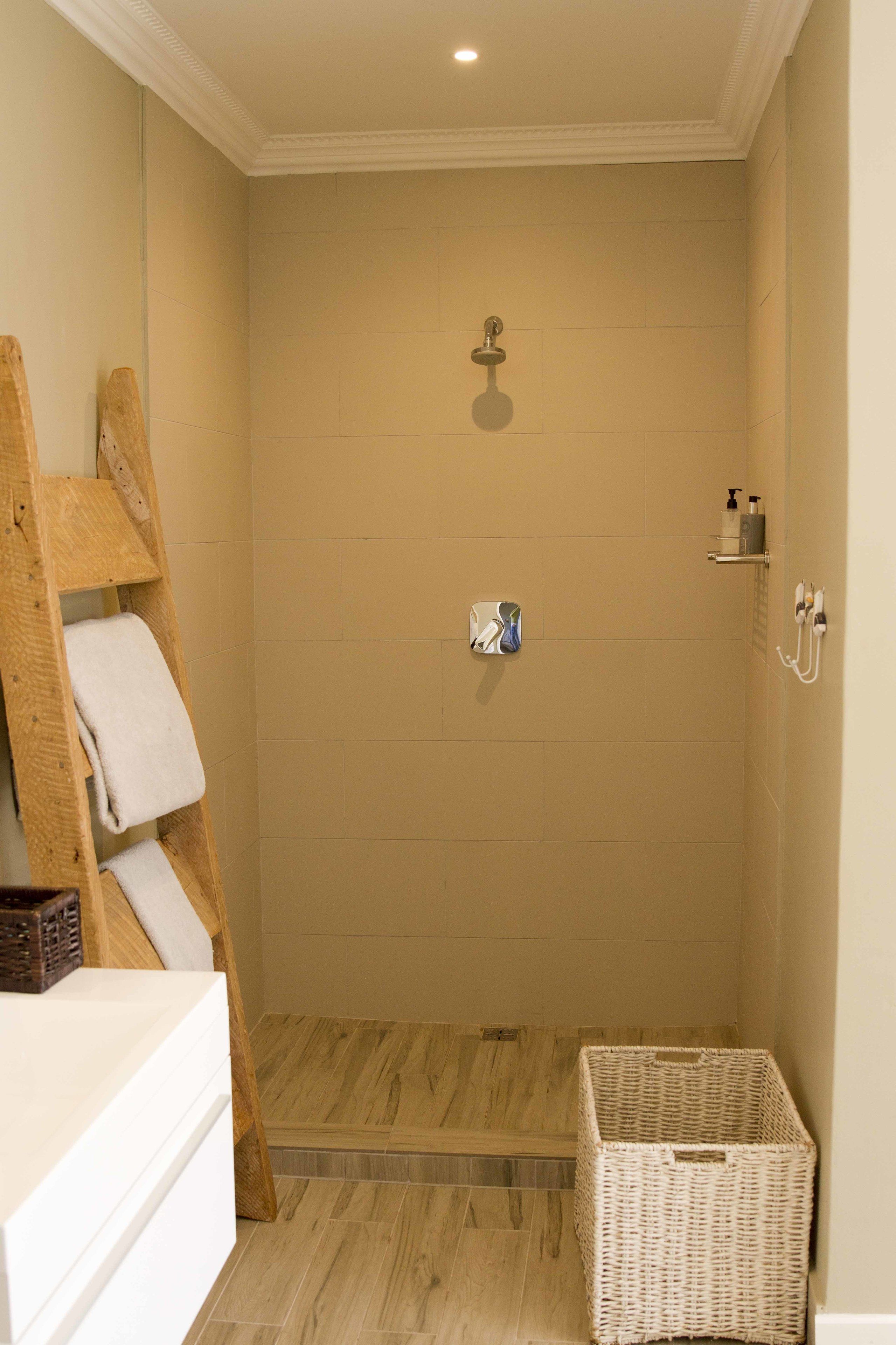 A shower area with a wooden ladder, a white towel, a wicker basket, and a showerhead.