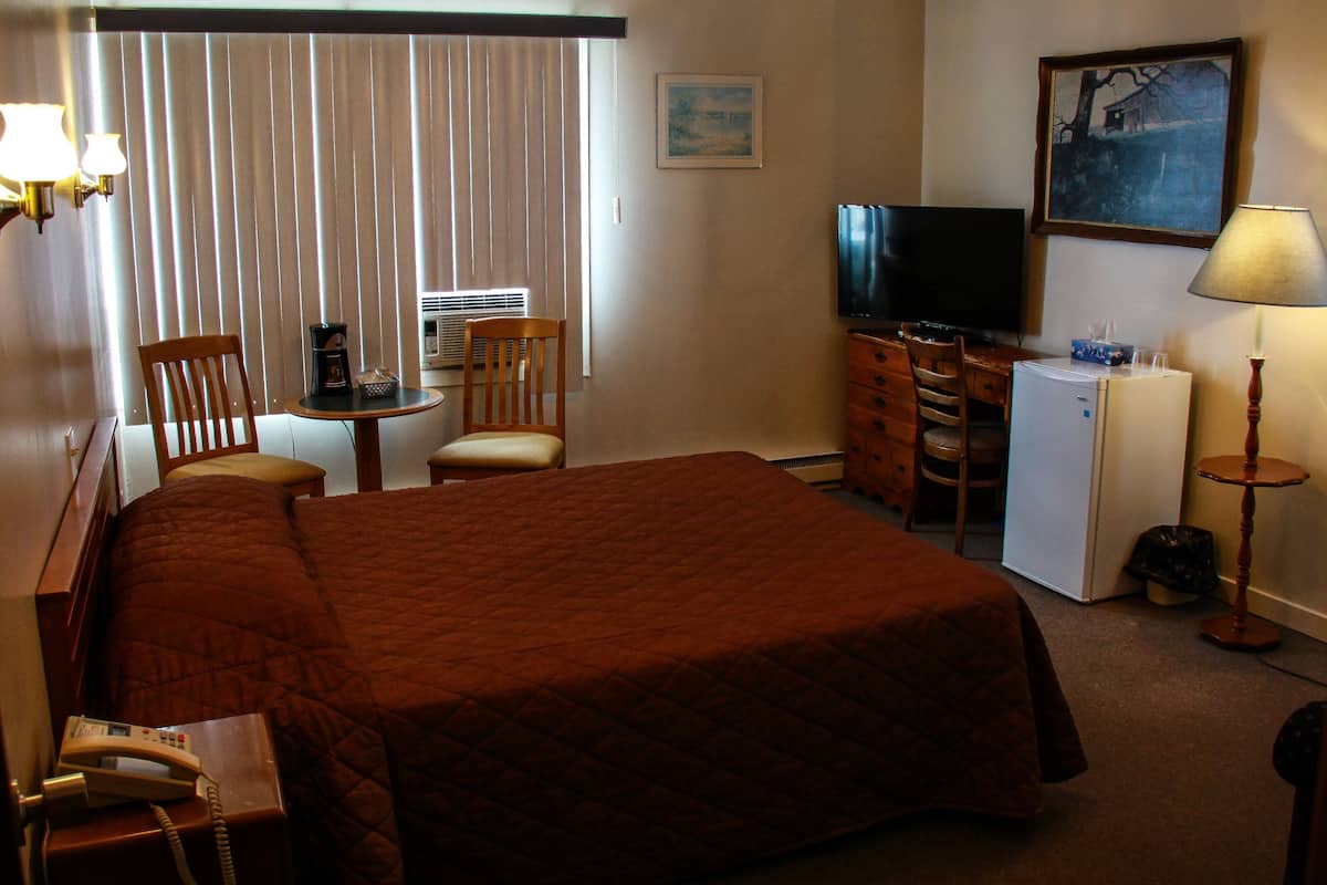 A hotel room with a large bed, a desk with a chair, a television, a refrigerator, and a lamp.