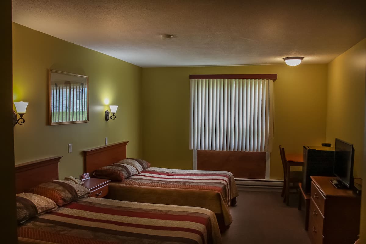 A hotel room with two beds, a desk, a chair, a television, and a window with blinds.