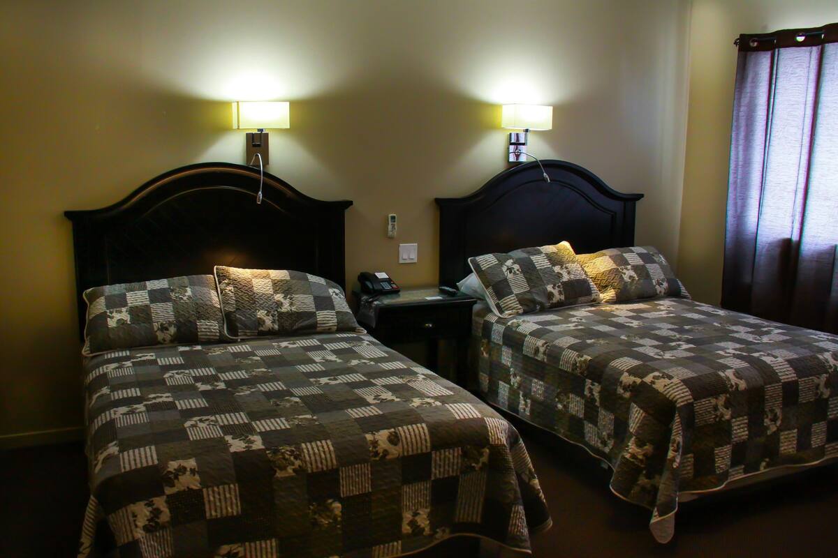 A hotel room with two beds, each with a quilted bedspread and matching pillows. There are bedside lamps and a telephone on the nightstand.
