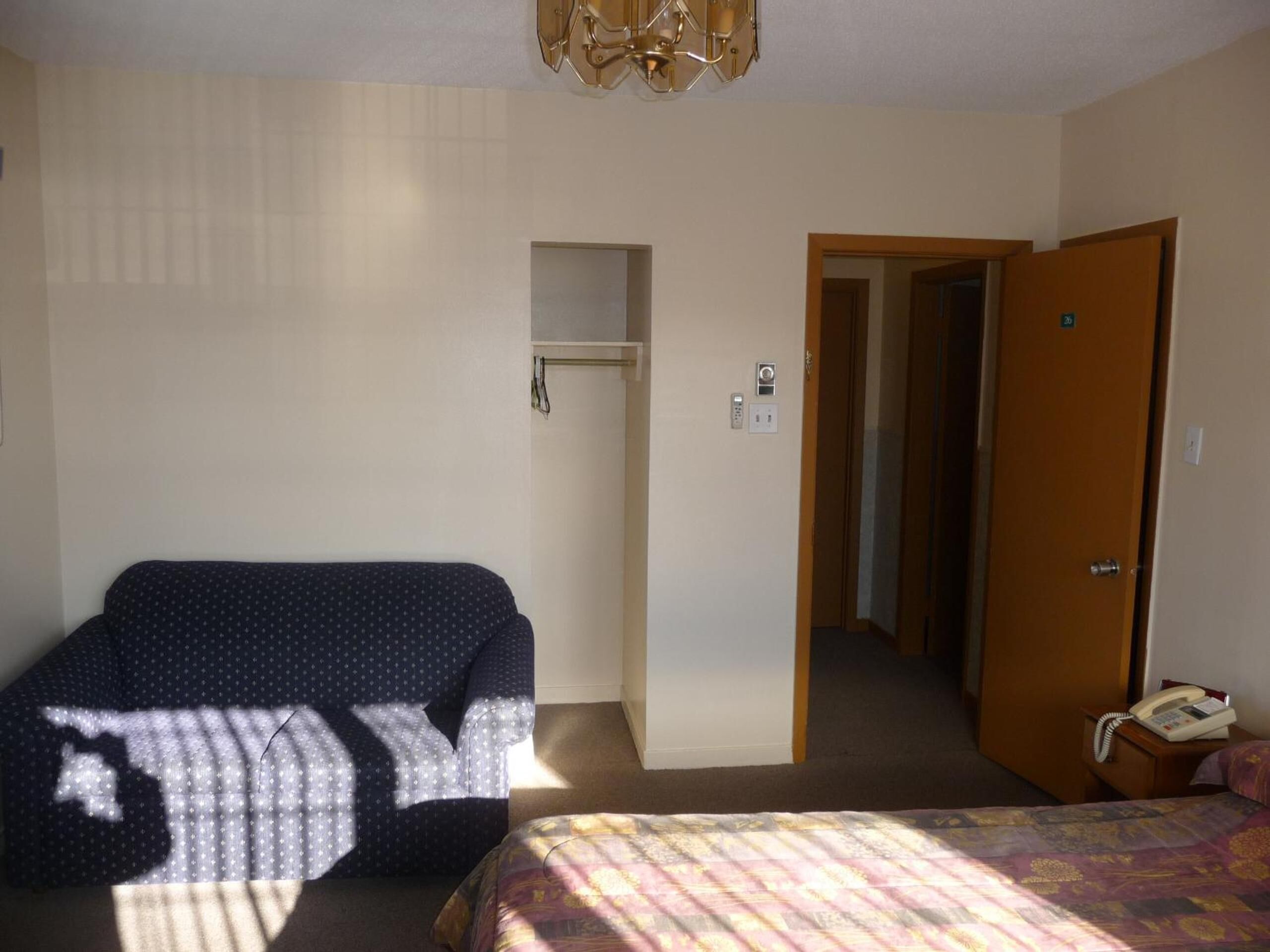 Una habitación de hotel con cama, una silla, un armario y una puerta que da a otra habitación.