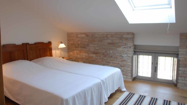 A bedroom with two beds, a skylight, a stone wall, and a door leading to a balcony.