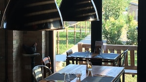 An outdoor dining area with two tables and chairs, a brick wall, and a view of greenery and mountains.