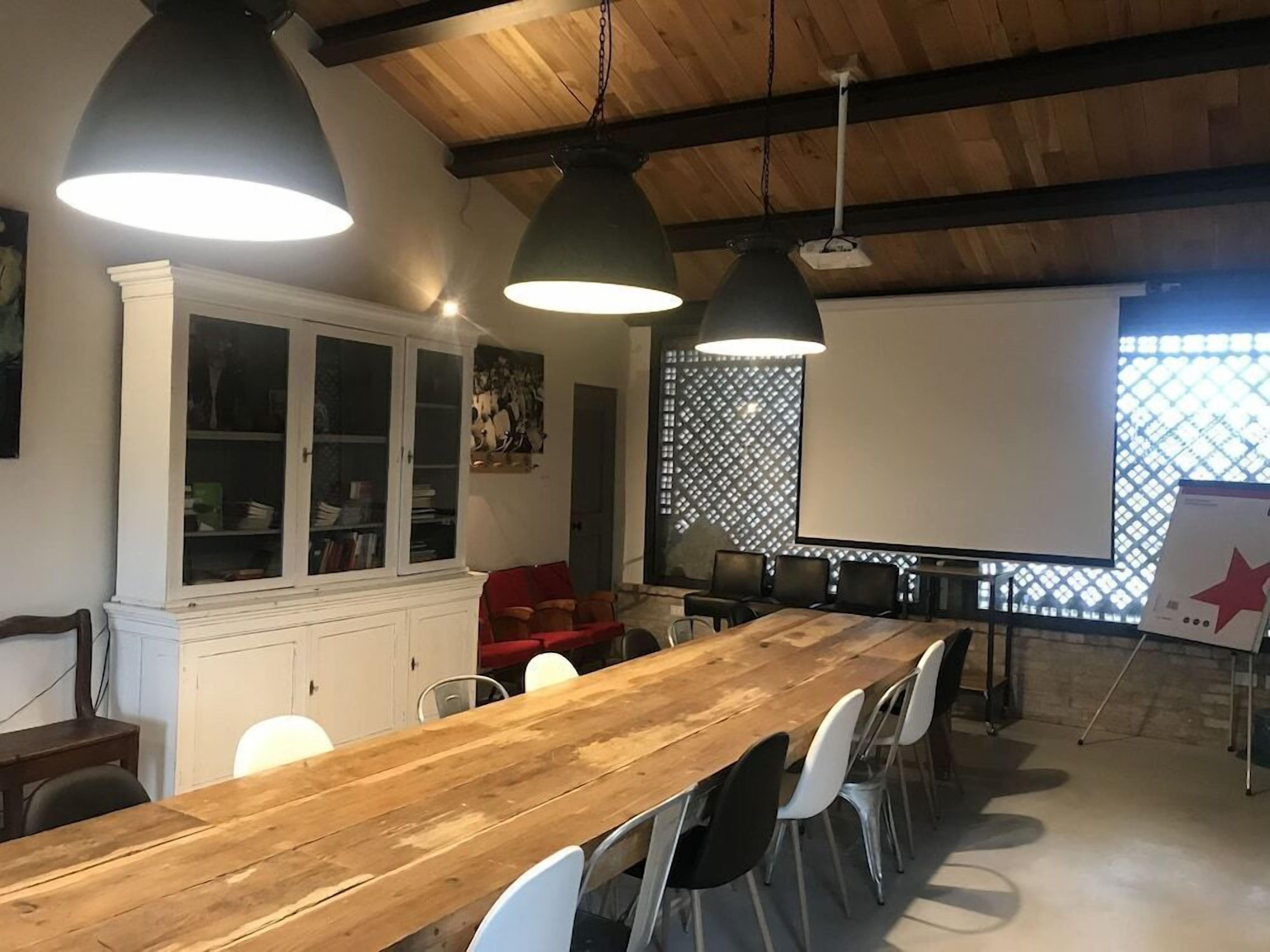 A conference room with a long wooden table, white chairs, and black pendant lights.