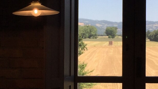 A room with a large window, a hanging light fixture, and a view of a rural landscape. - La Locanda Paradiso (Perugia)