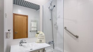 A bathroom with a white sink, a wooden door, a glass shower enclosure, and a white tiled wall. - Hotel Lamacaes (Braga)