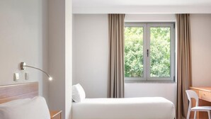 A hotel room with a bed, a desk, a chair, a window with curtains, and a wall-mounted lamp. - Hotel Lamacaes (Braga)