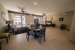 A spacious living area with a round glass table, blue cushioned chairs, a ceiling fan, and a balcony with curtains. - Palo Santo Galapagos Hotel (Puerto Ayora)