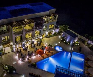 A multi-story hotel with a swimming pool, outdoor seating, and a well-lit patio area. - Palo Santo Galapagos Hotel (Puerto Ayora)
