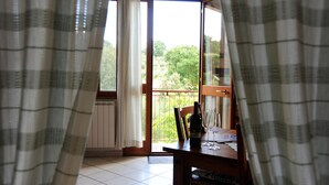 A room with a wooden table, a chair, a bottle, and a glass. There is a window with curtains, and a view of greenery outside. - Poggio delle Rose Tuscany Relais (Chianciano Terme)