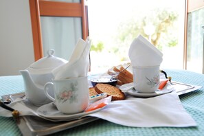 A breakfast tray with tea cups, a teapot, bread, and a small bowl of jam on a table near a window.