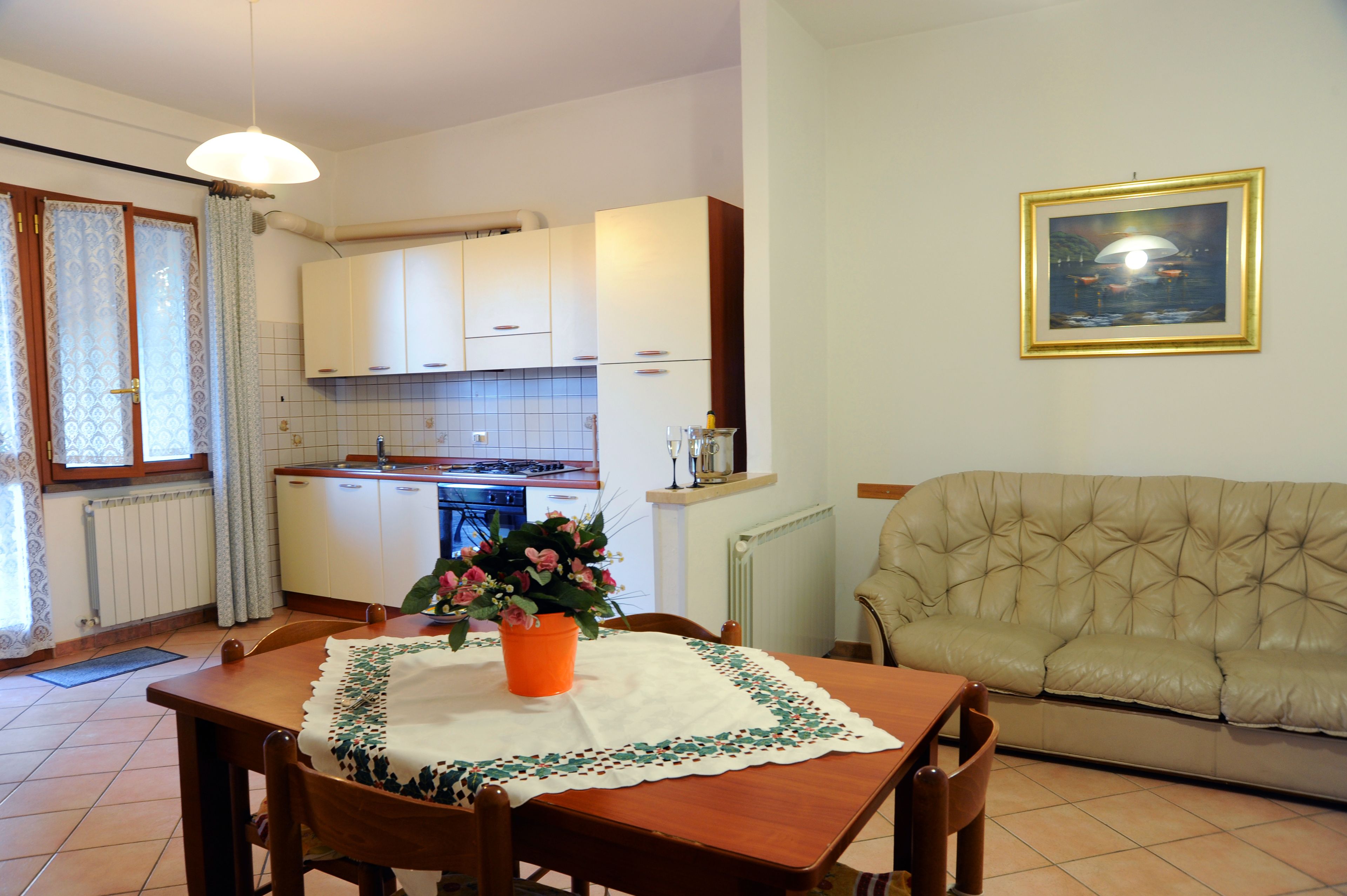 A dining area with a table set for two, a sofa, and a kitchen in the background.