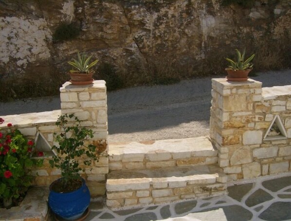 A stone wall with steps leading up to a terrace. - Athina Studios (Paros)