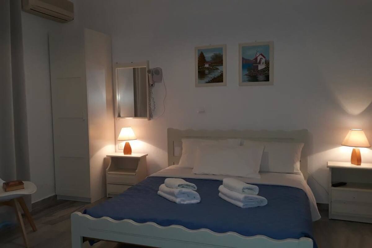 Un dormitorio con una cama, dos mesitas de noche, una silla, un espejo y dos cuadros en la pared.