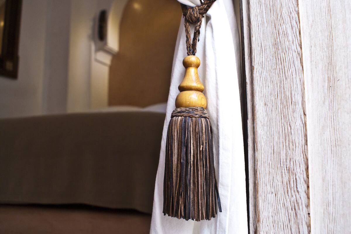 Een close-up van een houten kwastje dat hangt aan een gordijnroede in een kamer met een houten deur en een witte muur.