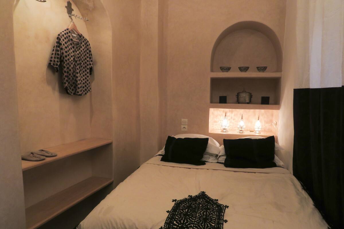 Een slaapkamer met een bed, een plank met een stippenhemd en een wandlamp.
