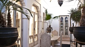 Une cour avec une table et des chaises, entourée de plantes en pot et d’une bibliothèque.