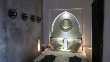 A bedroom with a bed, a wall-mounted clock, and a unique arched window.