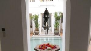 Une vue d’un espace piscine avec une table décorée de fleurs, entourée de plantes en pot et d’une lanterne suspendue.