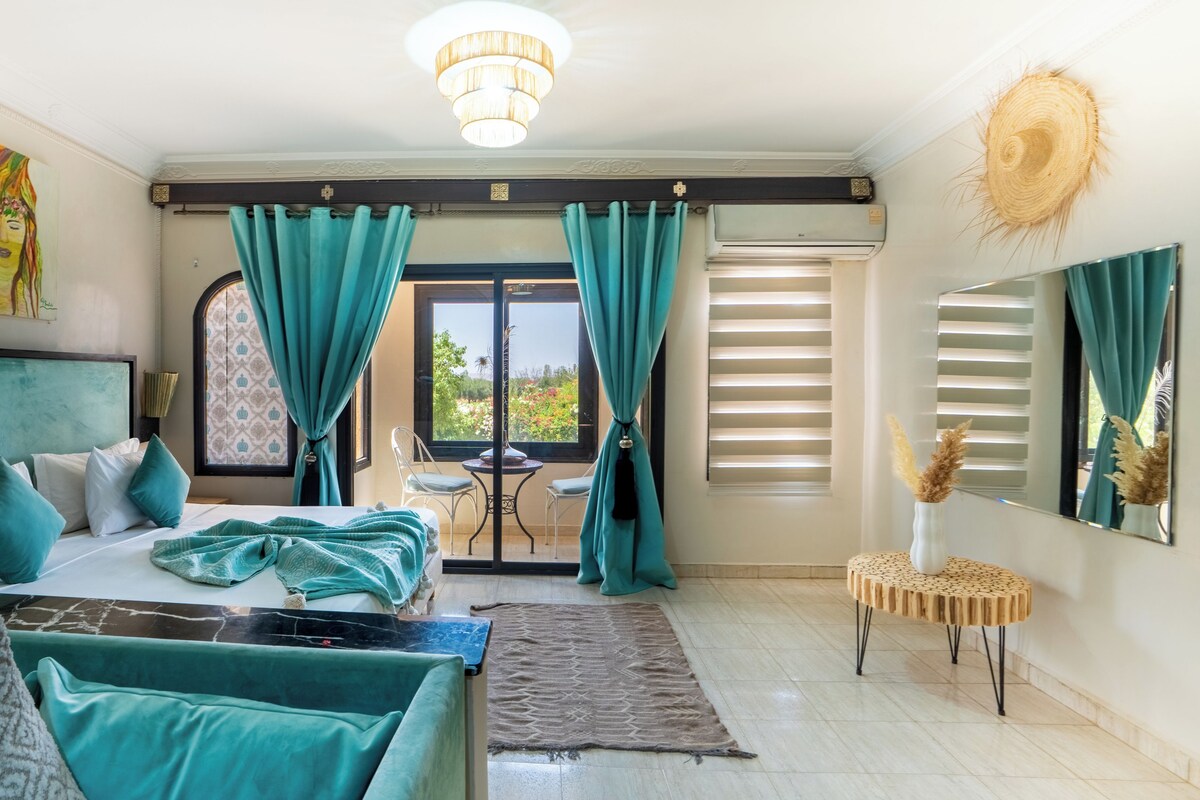 Une chambre d’hôtel avec un lit, une petite table, une chaise, une fenêtre avec des rideaux, un luminaire au plafond et une vue sur l’extérieur.