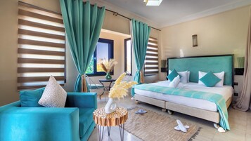 Habitación de hotel con una cama, un sofá, una mesita redonda de madera y vistas al exterior a través de amplias ventanas.