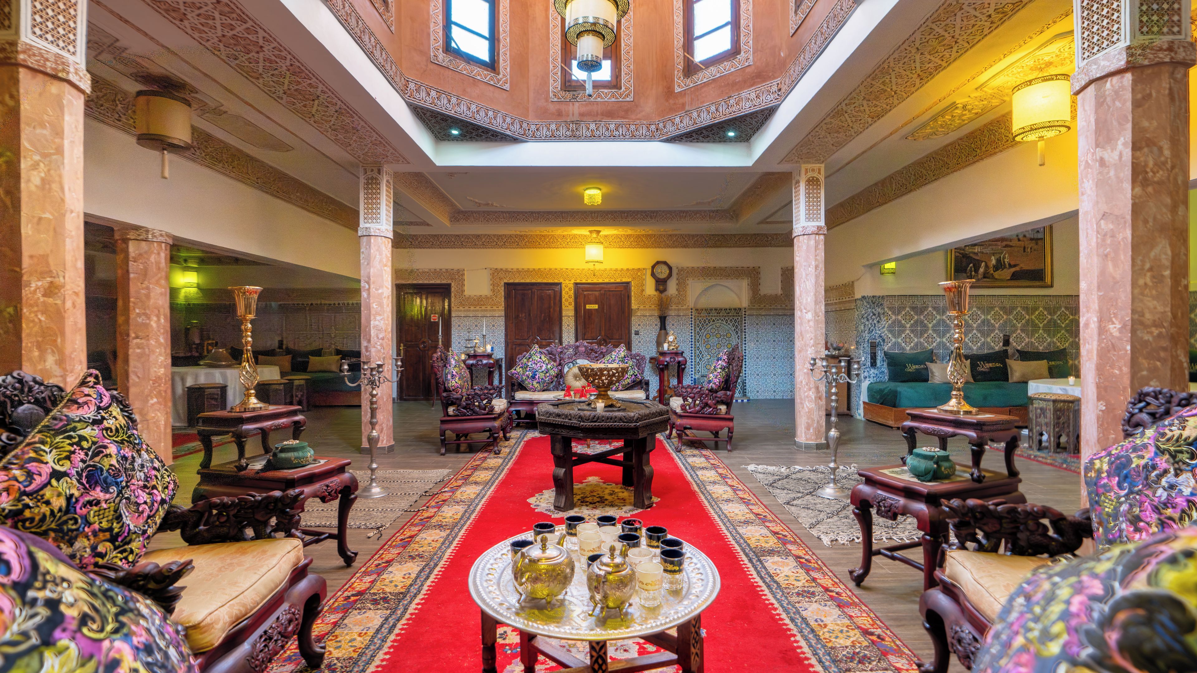 A traditional interior with ornate columns, a central coffee table with teapots, and patterned rugs.