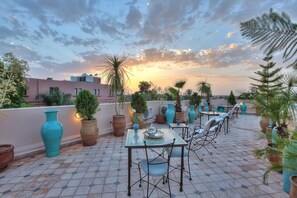 A rooftop patio with outdoor seating, potted plants, and a sunset view. - Dar Tasnime (Marrakech)