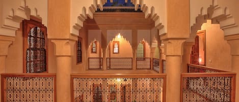An interior with arched doorways, a central decorative niche, and patterned metal railings.