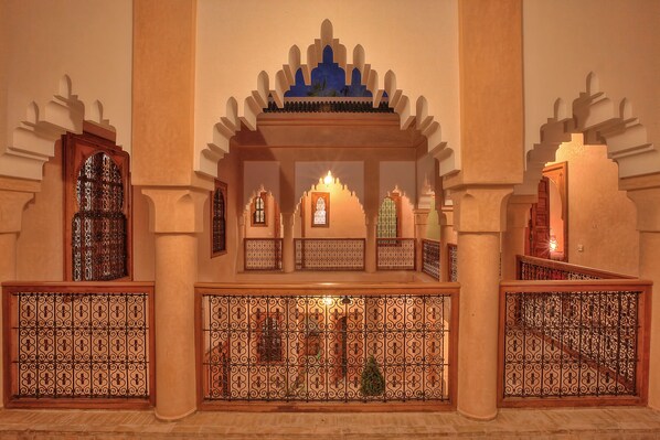 An interior with arched doorways, a central decorative niche, and patterned metal railings. - Dar Tasnime (Marrakech)