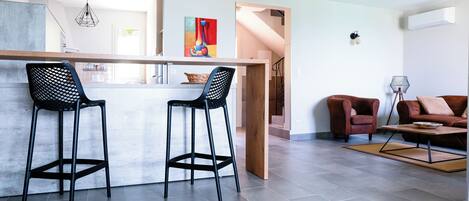 A modern kitchen with a bar area, two black barstools, a wooden stool, and a red abstract painting on the wall.