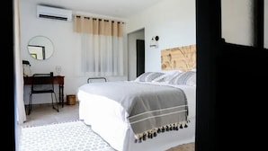 A bedroom with a bed, a desk with a chair, a mirror, and a window with curtains.