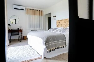 Une chambre à coucher avec un lit, un bureau avec une chaise, un miroir et une fenêtre avec des rideaux.