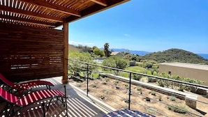 A balcony with a wooden ceiling, red striped chairs, and a view of a hilly landscape with a body of water in the distance.